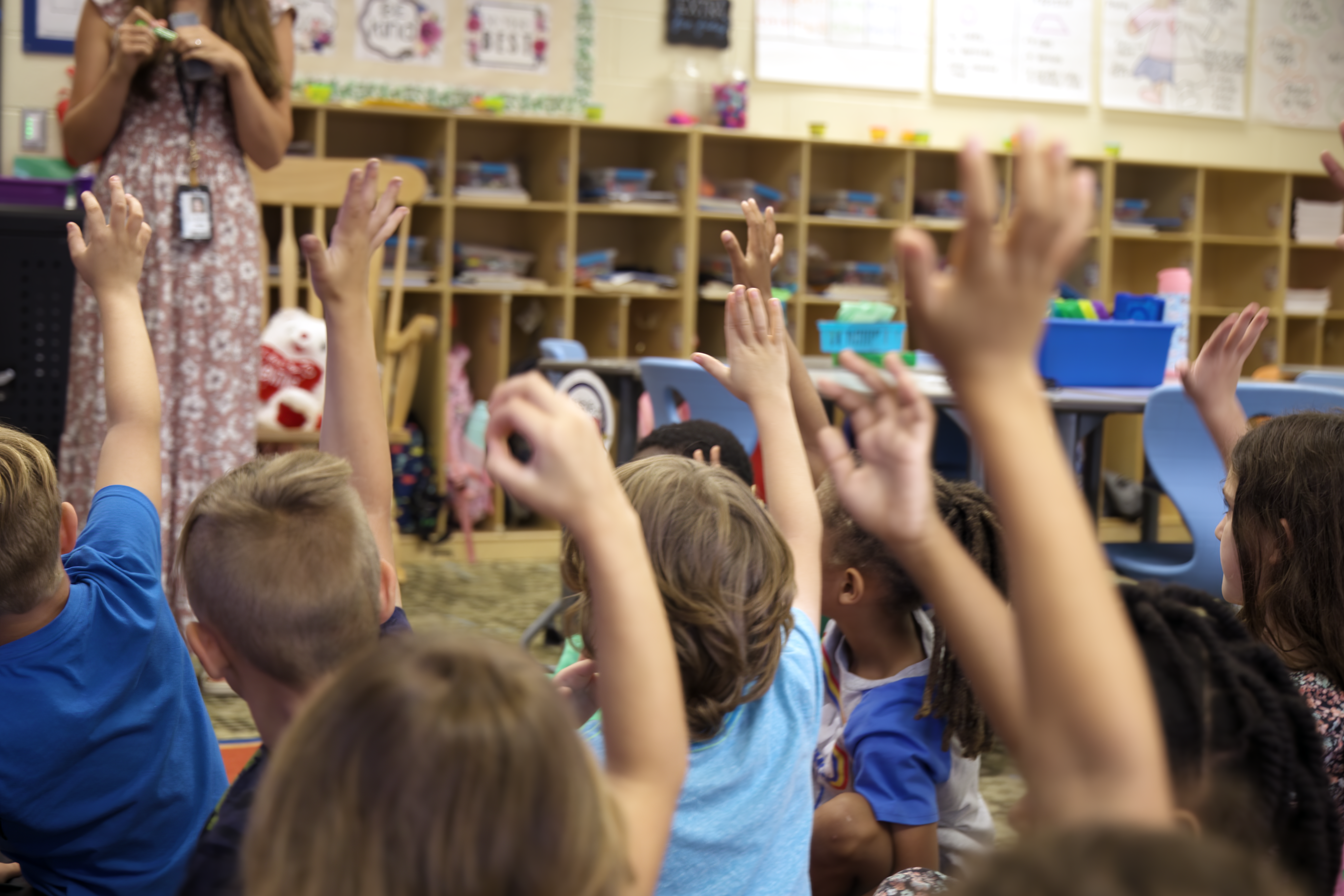 Classroom with many children with raised hands